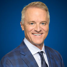 Headshot of Michael Mahoney in blue coat and smiling face.